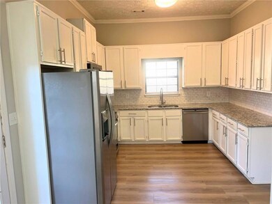 Kitchen featuring stainless steel appliances, light stone counters, white cabinets, backsplash, and ornamental molding