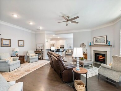 Living area with ceiling fan, wood finished floors, ornamental molding, recessed lighting, and a fireplace with flush hearth