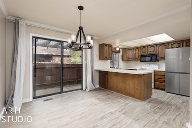 Kitchen featuring freestanding refrigerator, light countertops, white range with electric cooktop, a chandelier, and light wood-style flooring