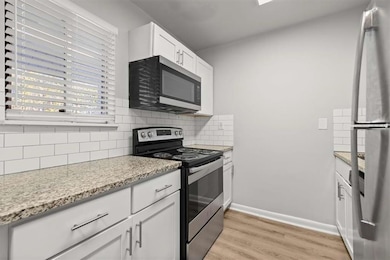 Kitchen featuring white cabinets, light stone counters, stainless steel appliances, light wood-type flooring, and decorative backsplash