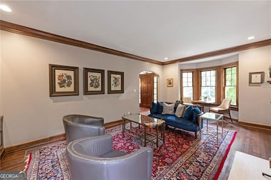 Living room with arched walkways, wood-type flooring, ornamental molding, and recessed lighting