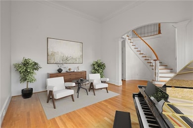 Living area with decorative columns, ornamental molding, light wood finished floors, and stairs