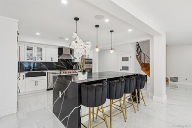 Kitchen featuring light marble finish flooring, a breakfast bar area, decorative backsplash, a large island with sink, and decorative light fixtures