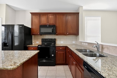 Kitchen featuring black appliances, light stone counters, tasteful backsplash, light tile patterned floors, and brown cabinetry