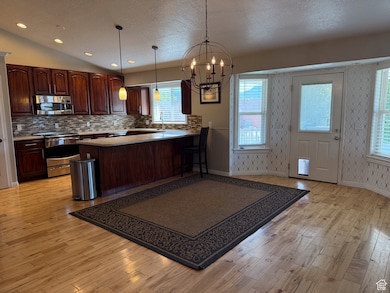 Kitchen with stainless steel appliances, light wood-style floors, a chandelier, tasteful backsplash, and a textured ceiling