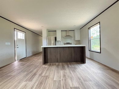 Kitchen featuring white cabinetry, light countertops, light wood-style flooring, exhaust hood, and ornamental molding