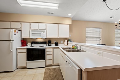 Kitchen featuring white appliances, light tile patterned floors, light countertops, white cabinets, and a peninsula