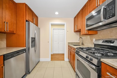 Kitchen featuring decorative backsplash, stainless steel appliances, brown cabinetry, light tile patterned floors, and recessed lighting