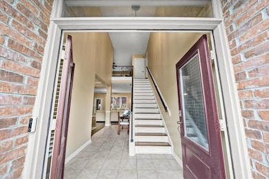 Foyer with light tile patterned floors, stairs, brick wall, and baseboards