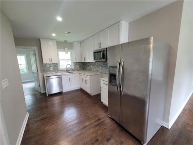 Kitchen featuring stainless steel appliances, decorative backsplash, light countertops, white cabinets, and dark wood-style floors