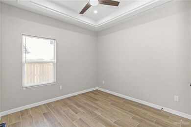Spare room with a raised ceiling, baseboards, light wood finished floors, a ceiling fan, and recessed lighting