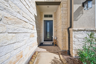 This photo showcases a modern, welcoming entryway with stone walls and a sleek, glass-paneled door. The pathway is lined with a tidy landscape, and a small bench sits near the entrance, adding a cozy touch.