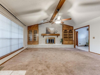 Unfurnished living room with a brick fireplace, a textured ceiling, light carpet, and ceiling fan