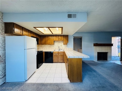Kitchen featuring light carpet, tile counters, black appliances, open floor plan, and light tile patterned floors