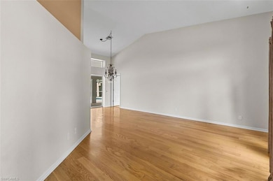 Empty room featuring light wood-type flooring, a chandelier, and high vaulted ceiling