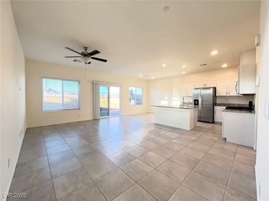 Kitchen with open floor plan, white cabinets, stainless steel fridge, light tile patterned flooring, and a center island with sink