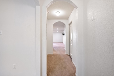 Corridor with arched walkways, light carpet, a textured wall, and a textured ceiling