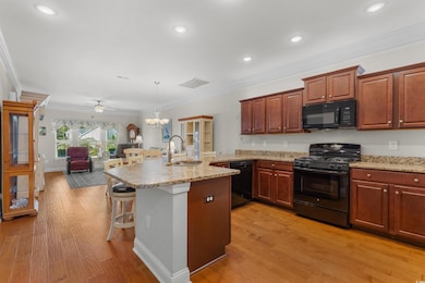 Kitchen featuring crown molding, black appliances, hanging light fixtures, ceiling fan, and a breakfast bar area