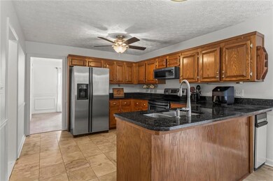 Kitchen featuring brown cabinetry, a peninsula, appliances with stainless steel finishes, a textured ceiling, and a ceiling fan