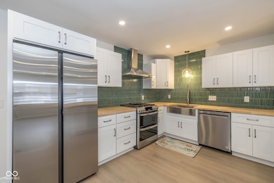 kitchen featuring white cabinetry, stainless steel appliances, wooden counters, wall chimney range hood, and recessed lighting