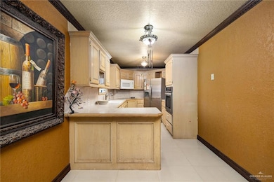 Kitchen with a textured wall, a peninsula, a textured ceiling, crown molding, and light countertops