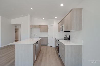 Kitchen with modern cabinets, light brown cabinetry, stainless steel appliances, light wood-type flooring, and a center island with sink