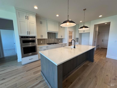 Kitchen with backsplash, white cabinetry, a large island, light stone counters, and light wood finished floors