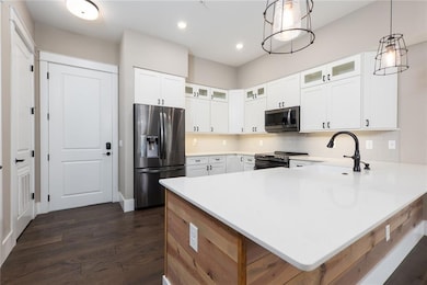 Kitchen featuring glass insert cabinets, fridge with ice dispenser, backsplash, pendant lighting, and white cabinets