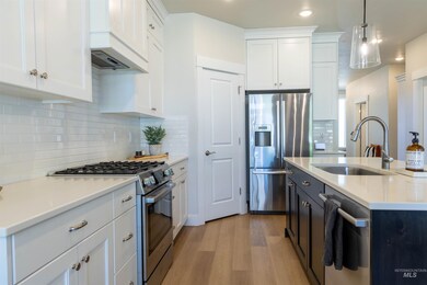 Kitchen with stainless steel appliances, light wood-style floors, light countertops, decorative light fixtures, and white cabinetry