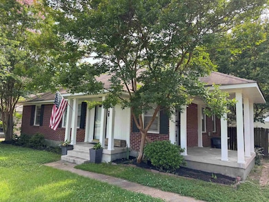 View of property hidden behind natural elements with brick siding and a porch