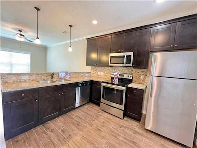 Kitchen featuring appliances with stainless steel finishes, dark brown cabinetry, ornamental molding, decorative light fixtures, and light wood-style flooring