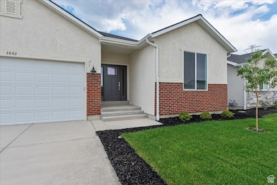 View of front of property with brick siding, stucco siding, a front yard, concrete driveway, and an attached garage