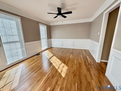 Spare room featuring ceiling fan, ornamental molding, wainscoting, light wood-type flooring, and a decorative wall