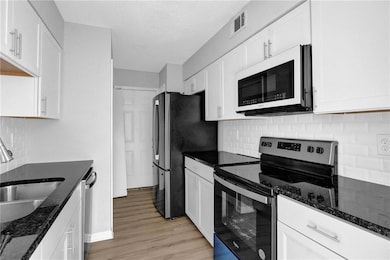 Kitchen featuring stainless steel appliances, white cabinetry, decorative backsplash, and light wood-style flooring