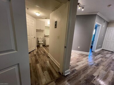 Corridor with crown molding, attic access, dark wood finished floors, a textured wall, and baseboards