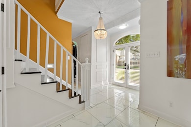 Foyer entrance featuring marble finish floors, stairway, french doors, a chandelier, and ornamental molding