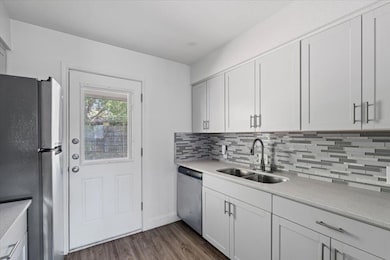 Kitchen with appliances with stainless steel finishes, dark wood-type flooring, backsplash, light stone countertops, and white cabinets