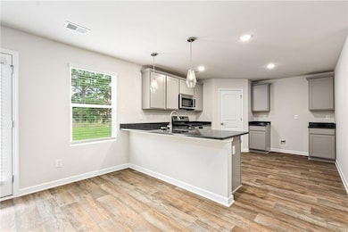 Kitchen with gray cabinets, recessed lighting, a peninsula, dark stone counters, and decorative light fixtures