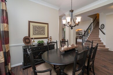 A pair of columns with intricate molding flank the entrance to the formal dining room, highlighted by  two windows shaded by 2 inch blinds, neutral paint, crown and chair rail molding, and an updated chandelier with a Venetian bronze finish.