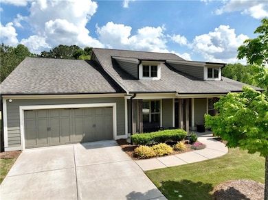 View of front of house featuring a shingled roof, an attached garage, a front lawn, covered porch, and driveway