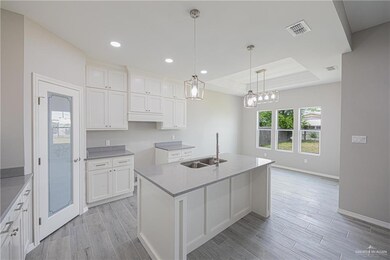 Kitchen with a tray ceiling, recessed lighting, an island with sink, decorative light fixtures, and white cabinetry