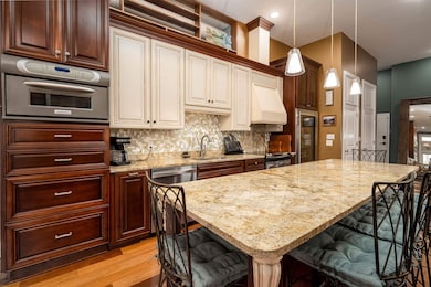 Kitchen with light wood-type flooring, a kitchen bar, premium range hood, decorative backsplash, and light stone counters