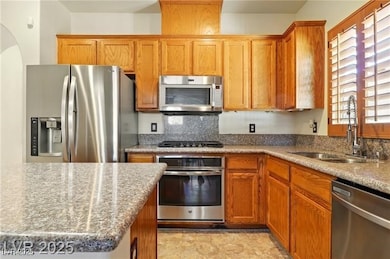 Kitchen featuring appliances with stainless steel finishes, brown cabinets, dark stone counters, and backsplash