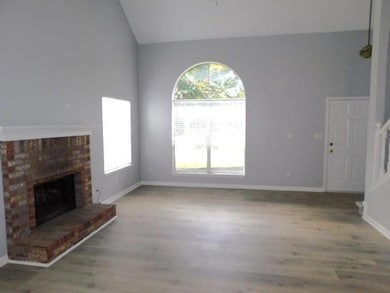 Unfurnished living room featuring lofted ceiling, wood finished floors, plenty of natural light, and a brick fireplace