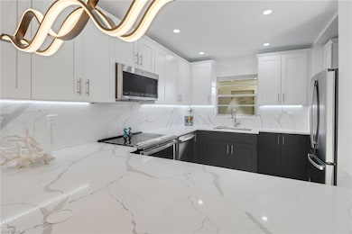 Kitchen featuring a sink, white cabinetry, light stone counters, and appliances with stainless steel finishes