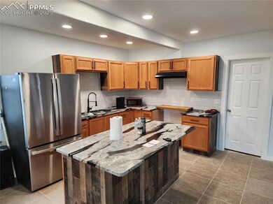 Kitchen featuring a sink, stone countertops, freestanding refrigerator, under cabinet range hood, and backsplash