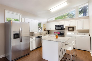 Kitchen featuring stainless steel appliances, washer and clothes dryer, a sink, white cabinets, and vaulted ceiling