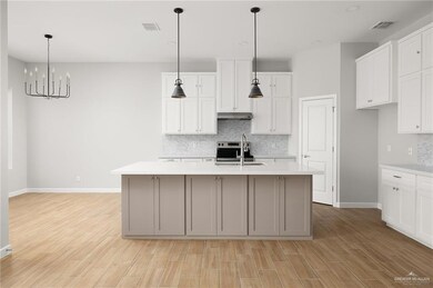 Kitchen with light wood-style floors, under cabinet range hood, visible vents, and a sink