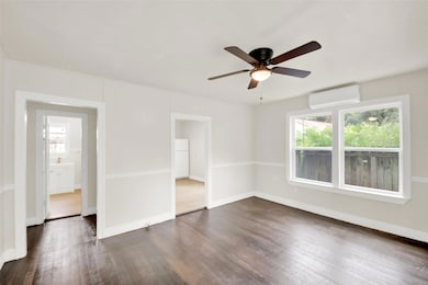 Unfurnished room featuring dark wood-type flooring, a wall mounted air conditioner, and a ceiling fan