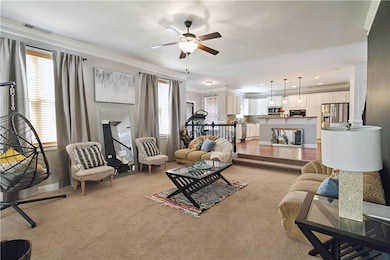 Living area with ceiling fan, plenty of natural light, light colored carpet, and crown molding